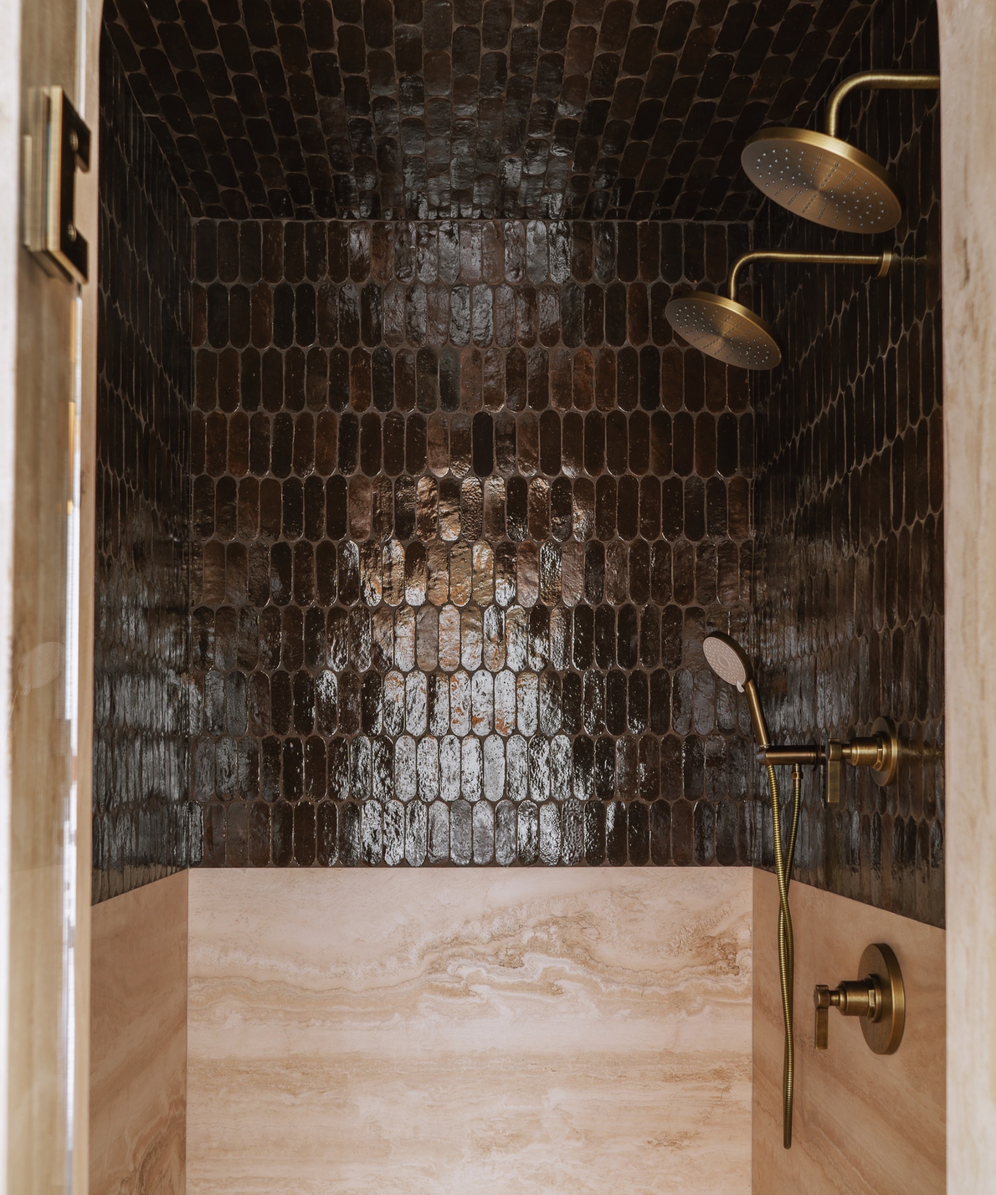 A shower nook with dark pill tiles across the ceiling and upper half of the walls, and marble slabs across the lower half
