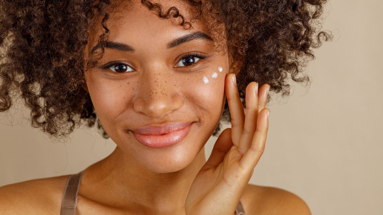 best eye cream - close up of a black woman with curly hair applying eye cream