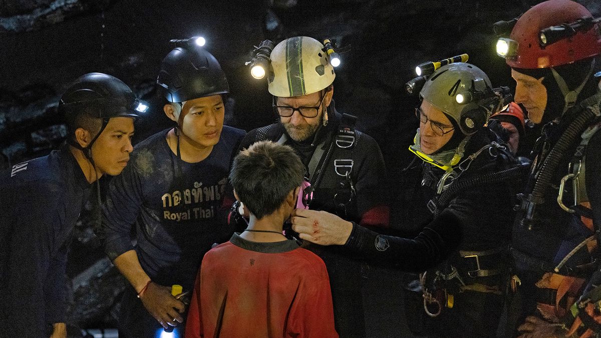 A group of divers stand around a small boy in the movie Thirteen Lives