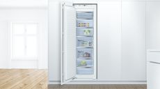 Bosch Serie 6 GIN81AEF0G Built-In Freezer, one of the best upright freezer options, in a white modern kitchen with a wooden floor