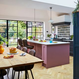Kitchen diner with pink and blue units, kitchen island, white worktop and walls, wooden flooring, large sky lights and French doors to garden