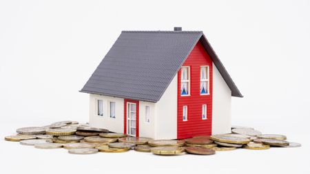 A house sits on top of a pile of coins.