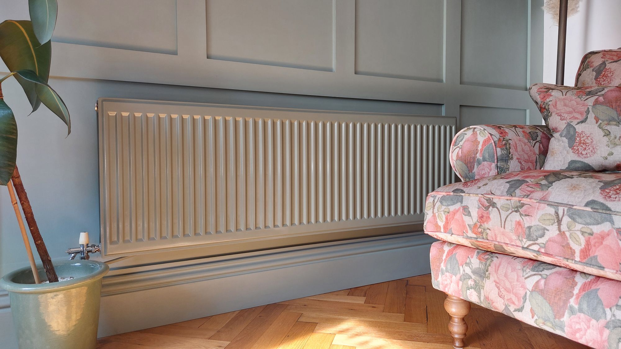 silver radiator in living room with blue panelled walls, wooden flooring and pink floral armchair