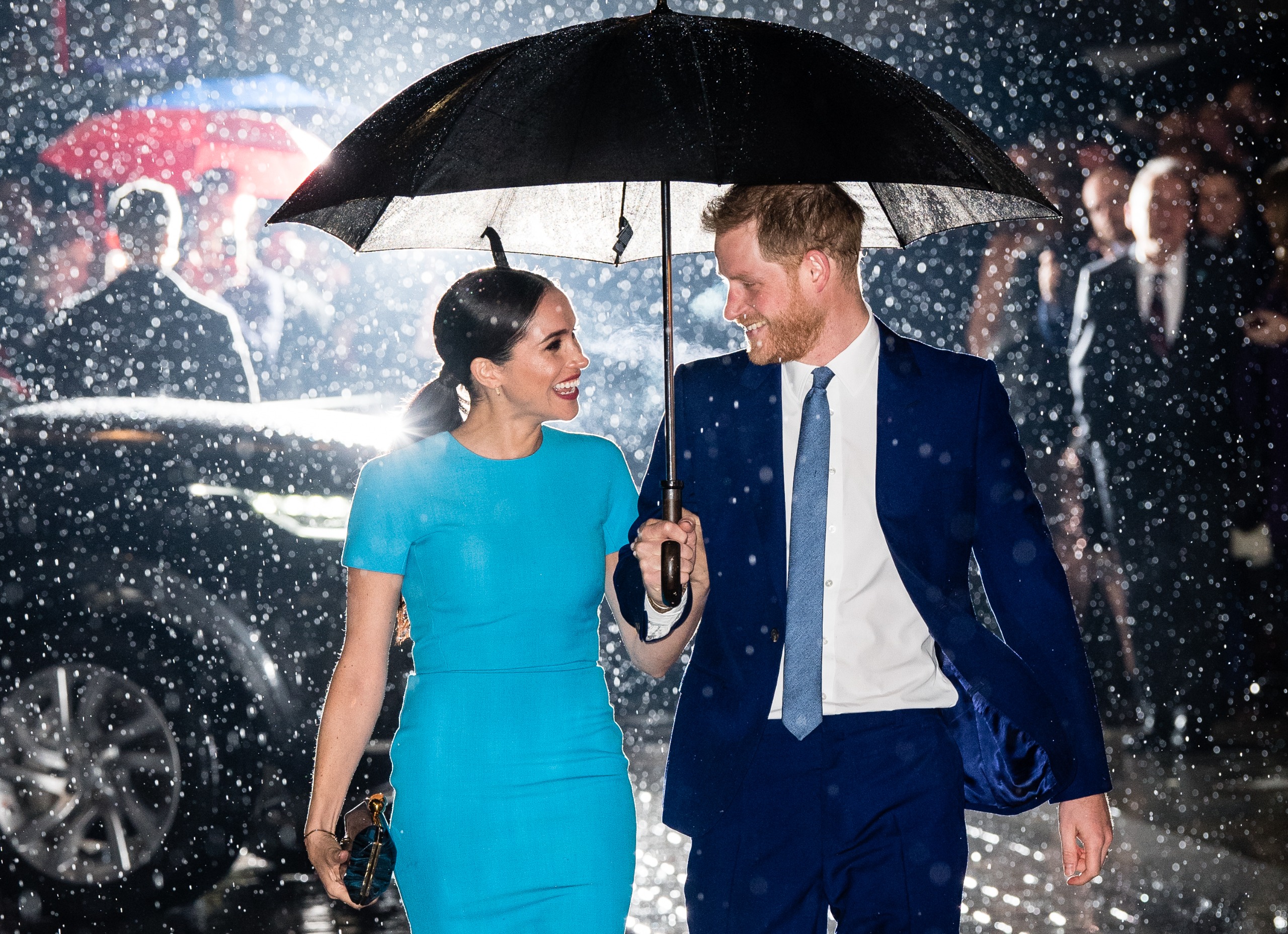 Prince Harry and Meghan Markle walking under an umbrella in the rain