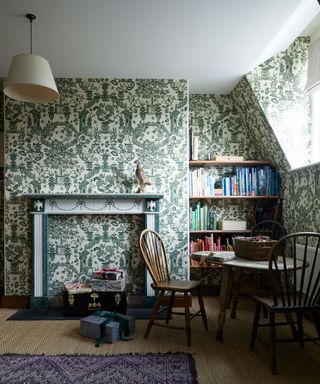 Room with green and white dramatic wallpaper, green and white fire mantelpiece, jute flooring and presents wrapped on floor by table and chairs.