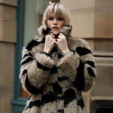 Model wearing a black and light brown fur coat sold at Warehouse holding the collar up to her face