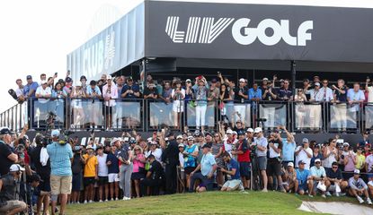 Cameron Smith hits a chip shot in front of a LIV Golf banner and fans