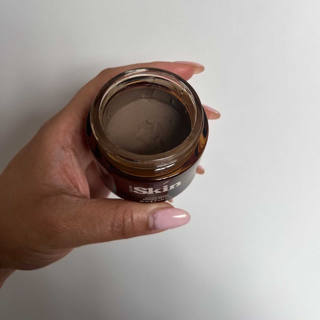 A close-up of Digital Beauty Ecom Editor, Aleesha Badkar holding an open jar of the Soho Skin Detox Clay Face Mask, in front of white background