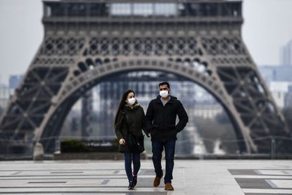 People wear masks in front of the Eiffel Tower.