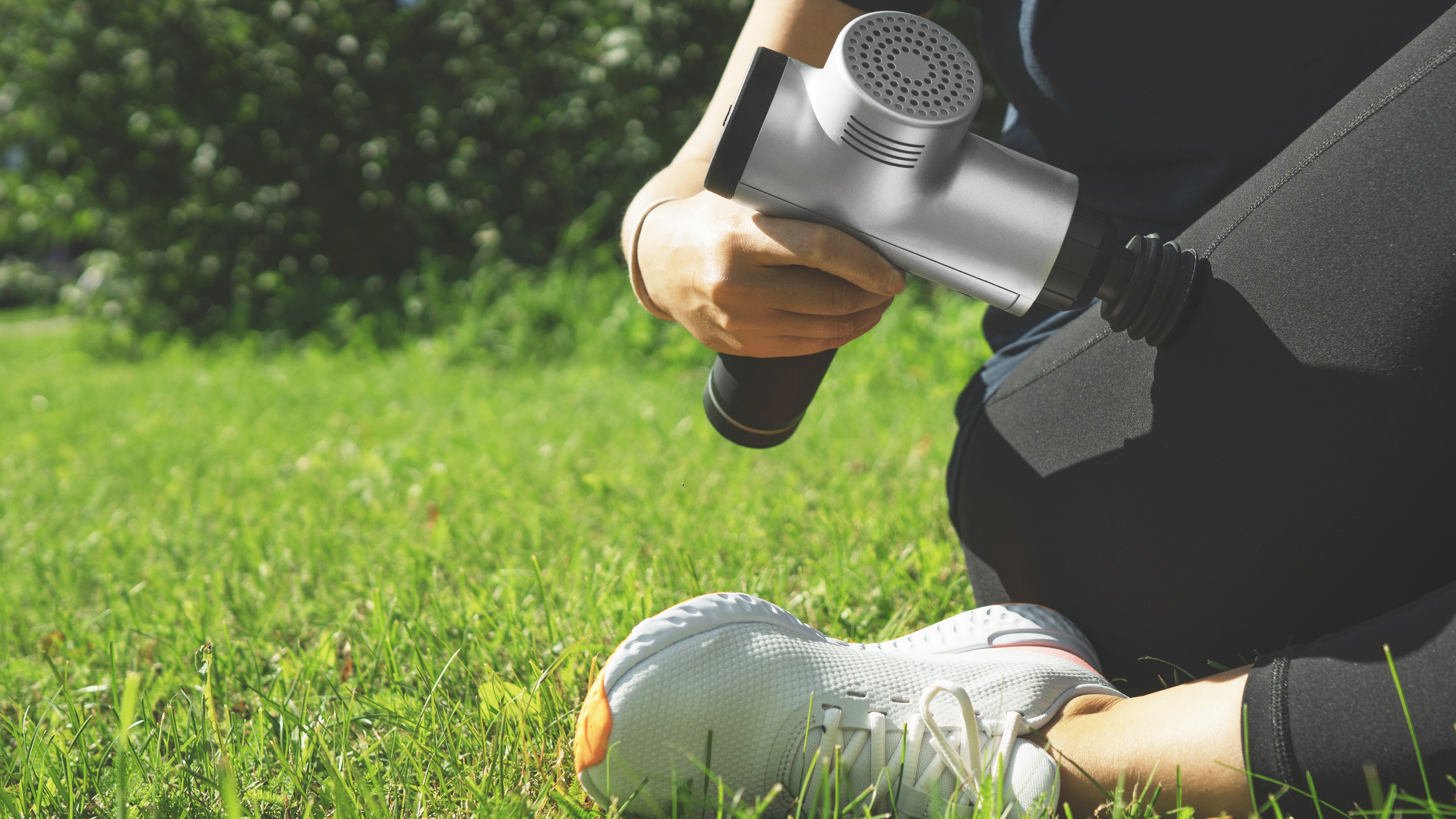 Woman sitting on grass using massage gun on leg