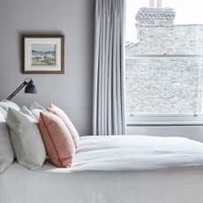 A bedroom with a bed in front of a large sash window. The bed has white and orange pillows and a white duvet cover