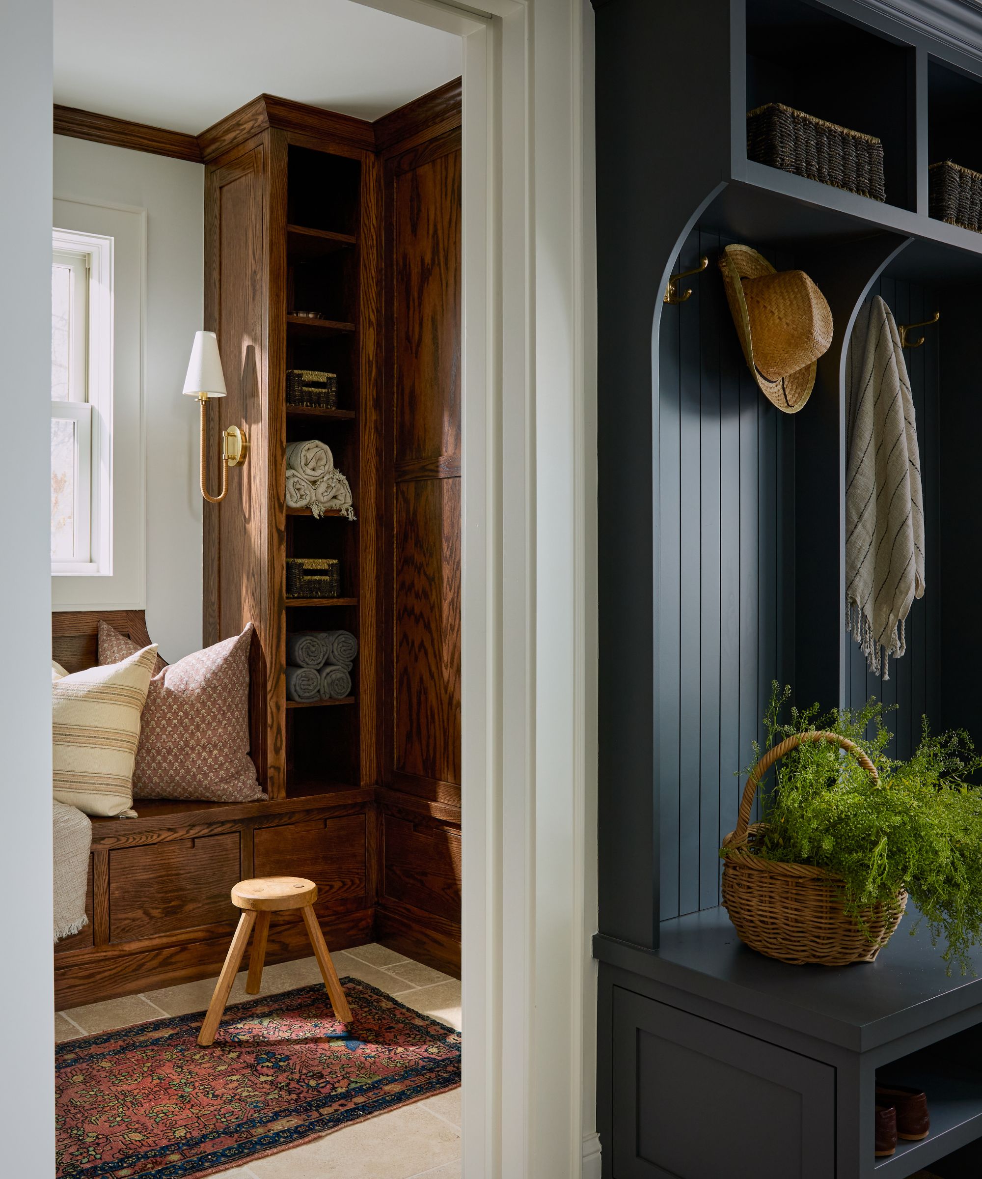entryway with a dark navy coat stand with hooks for hats and coats, a basket with foliage and a doorway looking into a dark wood boot room with neutral walls and vintage rug