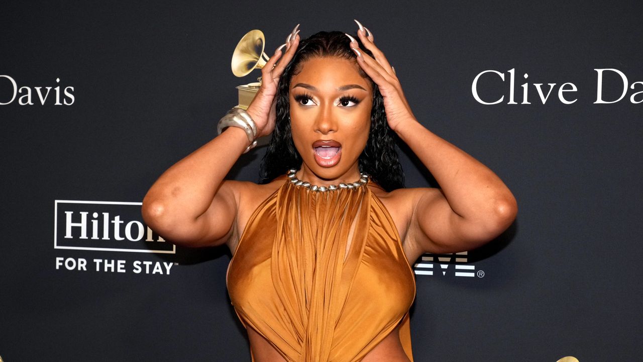 Megan Thee Stallion stands in front of a step and repeat with long nails