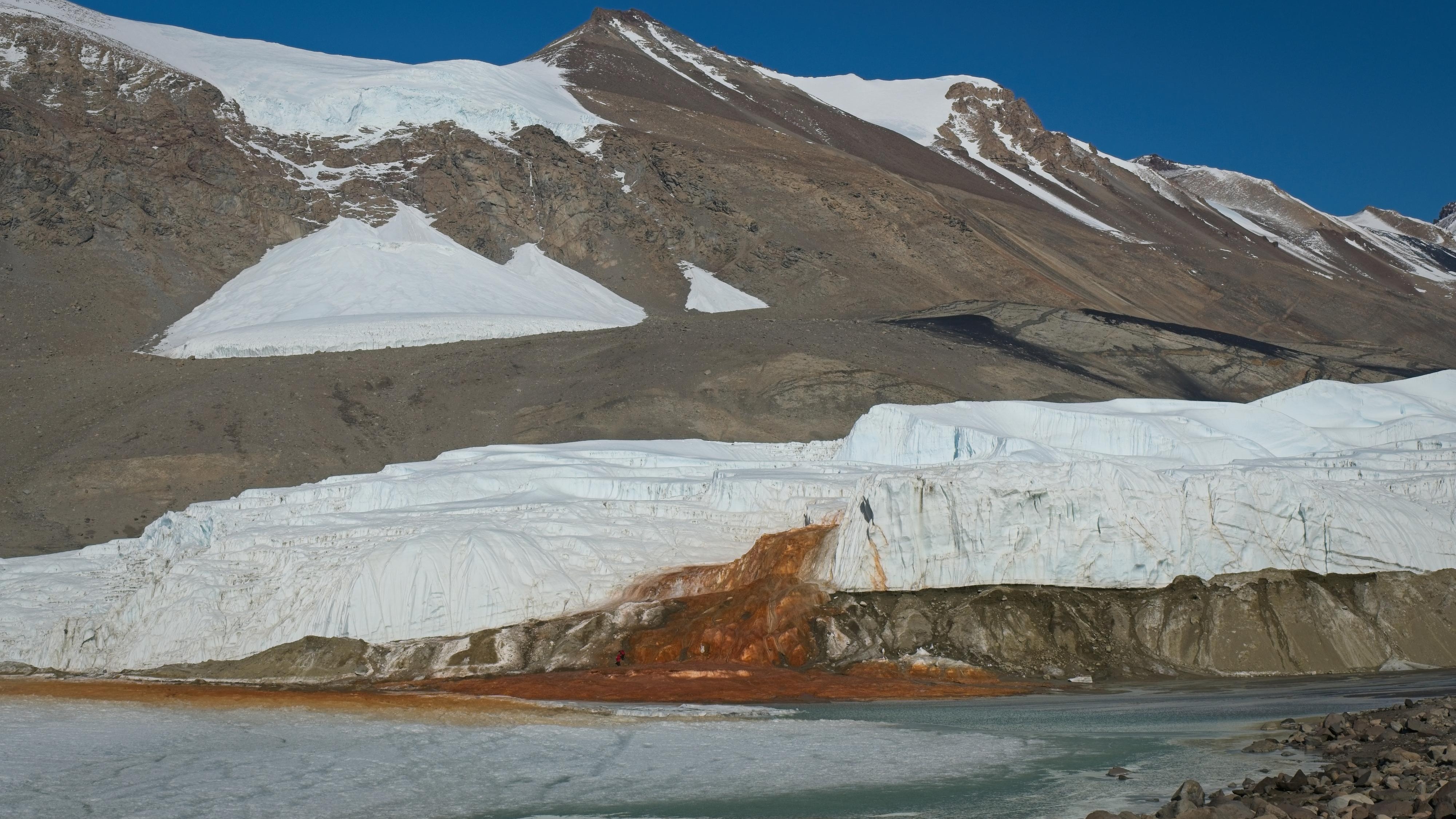 View of a red waterfall emerging from a glacier and flowing into a lake