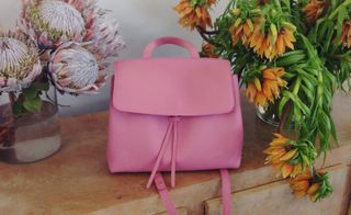 Pink satchel and backpack in one on countertop next to proteas and sunflowers