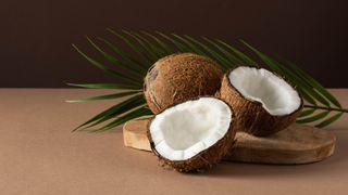 Two coconuts on a wooden board with one cut in half