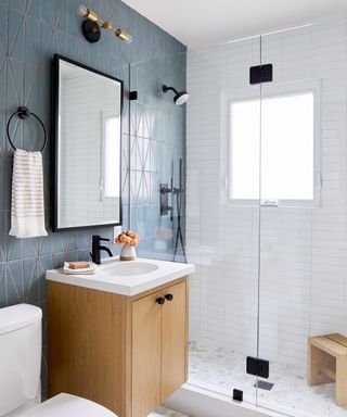 A shower room with blue triangular wall tiling, white oak cabinet and white tiling inside the cubicle