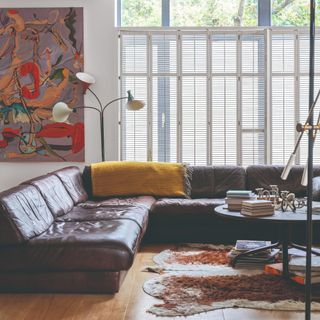 A living room with a large brown leather corner sofa, an animal skin-style rug and a colourful painting on the wall