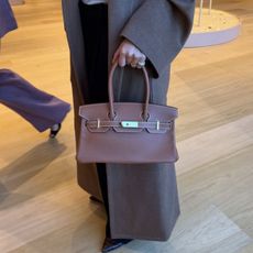 A woman wearing a mole brown coat carrying an Hermes handbag