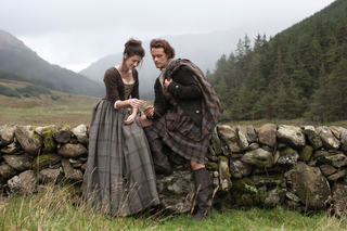 Caitriona Balfe sitting on a stone wall in in scene from 'Outlander'