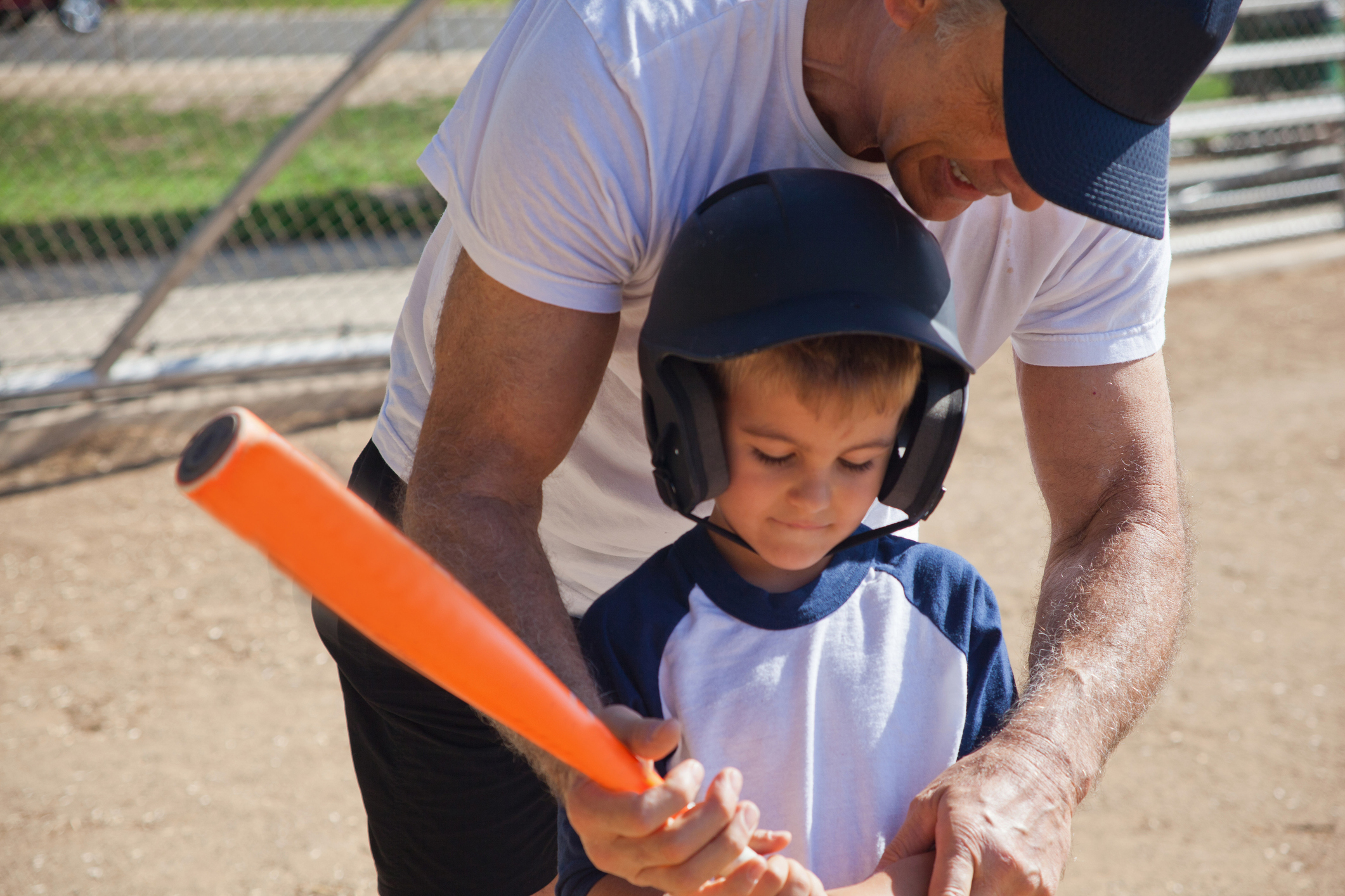 A grandfather is teaching his grandson how to bat at baseball.