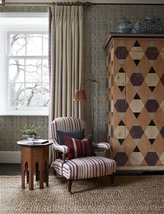 A bedroom with patterned wallpaper, a painted wardrobe with a geometric design, and a striped accent chair