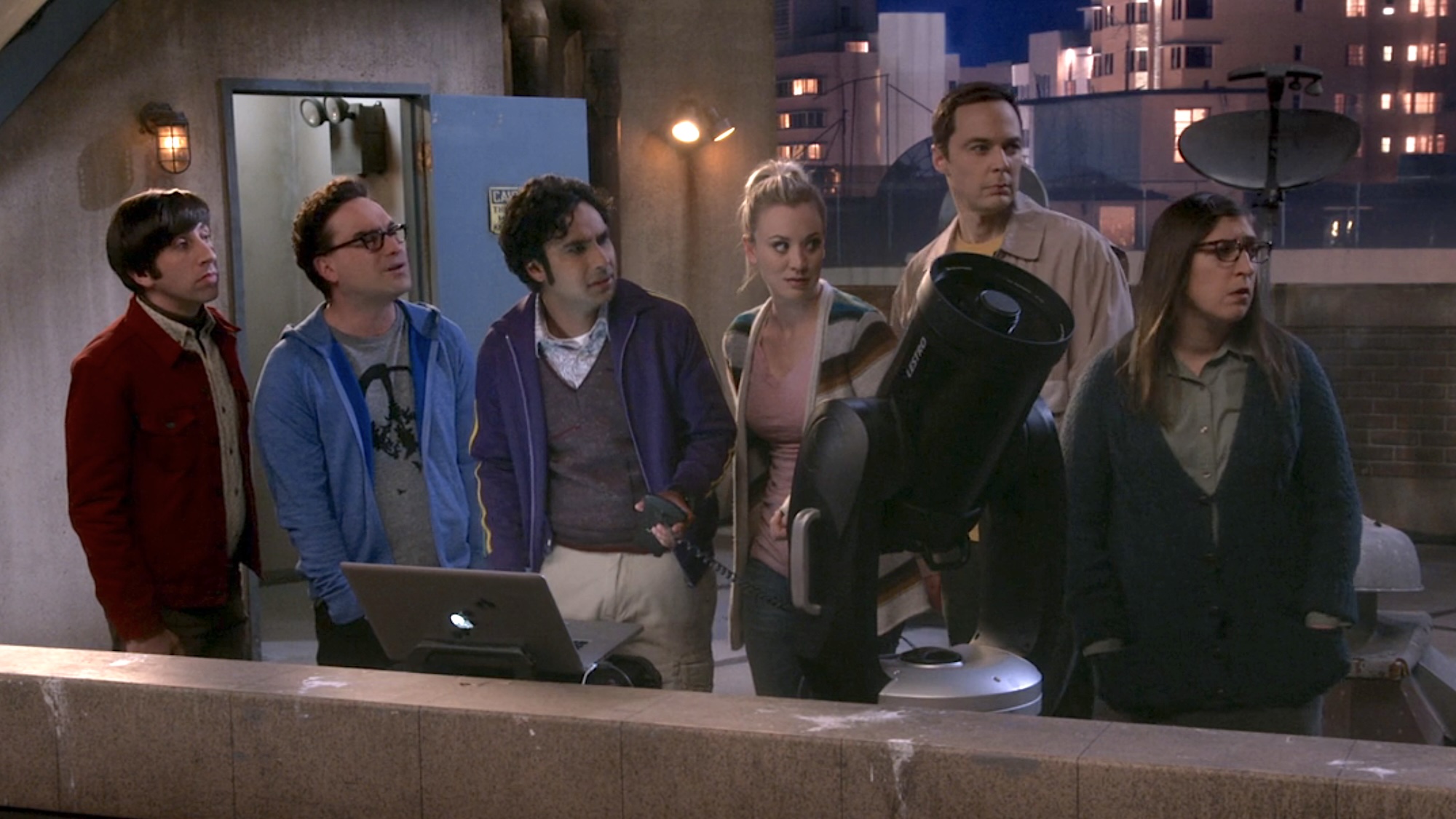 Howard, Leonard, Raj, Penny, Sheldon and Amy standing on the roof of their apartment building in front of an open laptop and a telescope, with everyone looking off-camera at Staurt