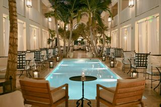 The inner courtyard of Cara Hotel features a heyday Hollywood-inspired atmosphere with a central, illuminated pool, wrought iron chairs covered in soft white linen cushions, and mid-century modern furniture, all lit up by candlelights.