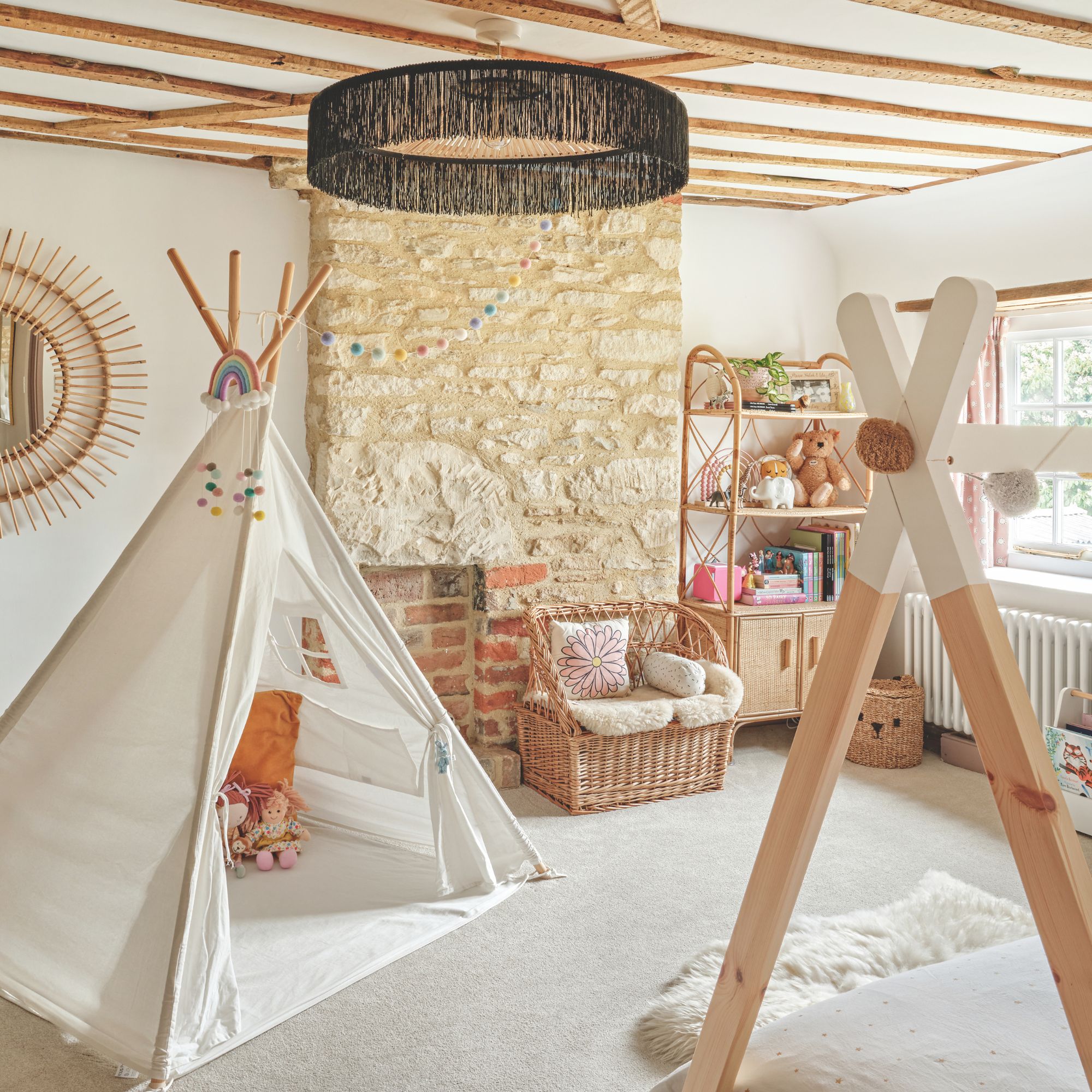 Cottage kids bedroom with wooden ceiling beams, large stone statement wall and white carpet. Large white teepee and bamboo furniture