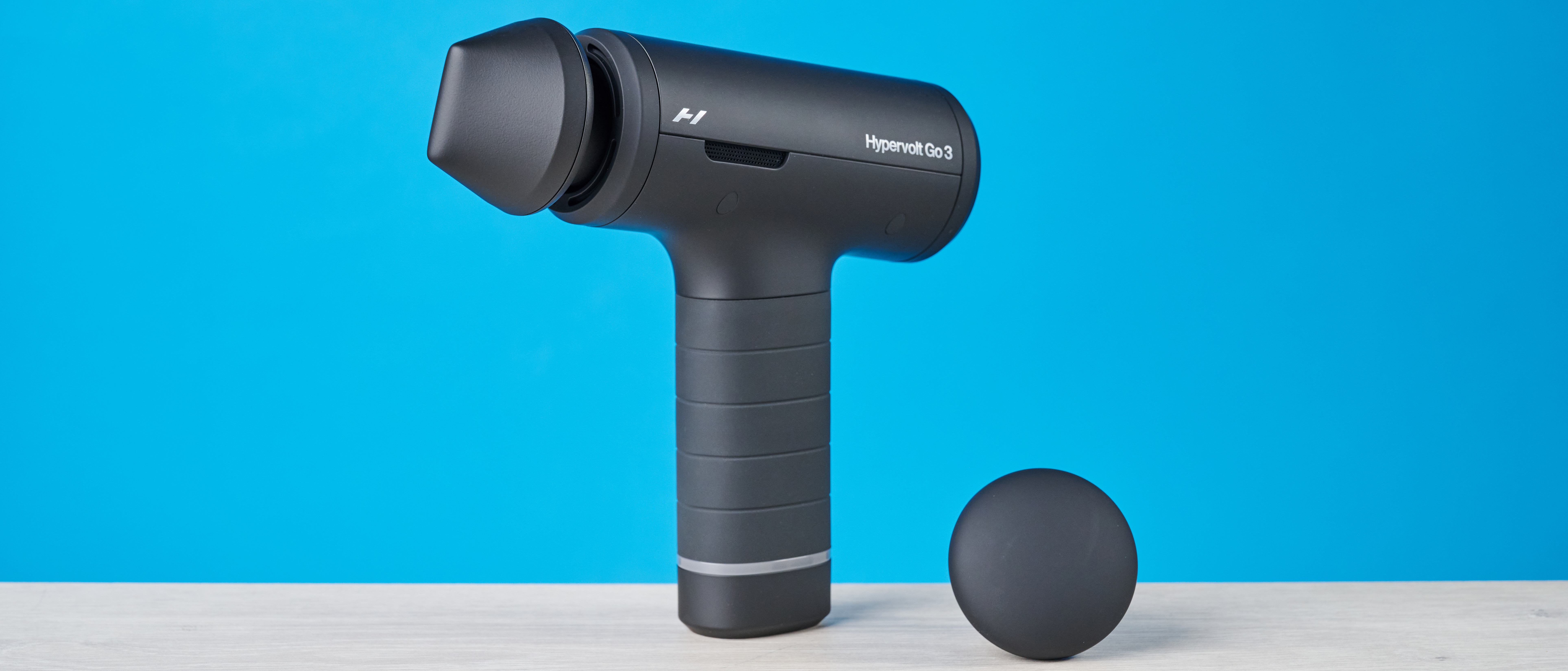 Hyperice Hypervolt Go 3 massage gun photographed in front of a blue background