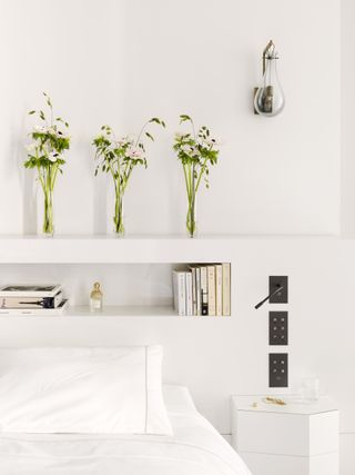 white bedroom with overhead storage, wall light, contemporary side table, white bedding