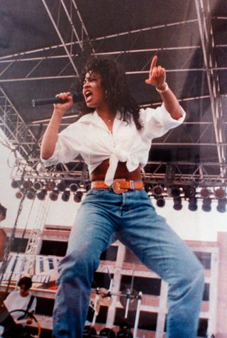 Tejano singer & future murder victim Selena singing into mike on outdoor stage.