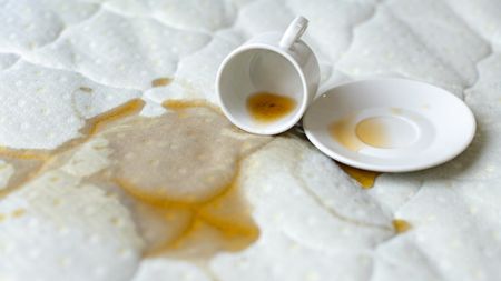 A cup of coffee spilled on a white mattress