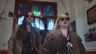 Maggie and Eddie (played by Nicola Coughlan and Lydia West) strut down a corridor in sunglasses and fur coats in Big Mood