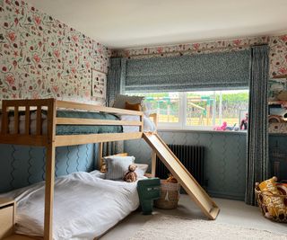 wooden bunkbeds in room with blue roman blinds, curtains and red and blue floral wallpaper