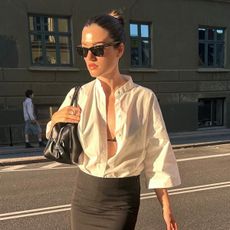 @iliridakrasniqi wearing a white button-down shirt tucked into a double-layer black pencil skirt with sandals and a black purse.