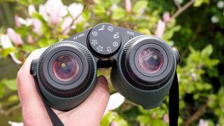 Swarovski Optik AX Visio binoculars held in a hand in front of some bushes
