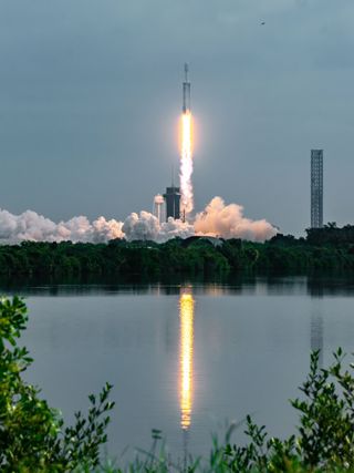 a rocket launches as the flames from the engines reflect in water