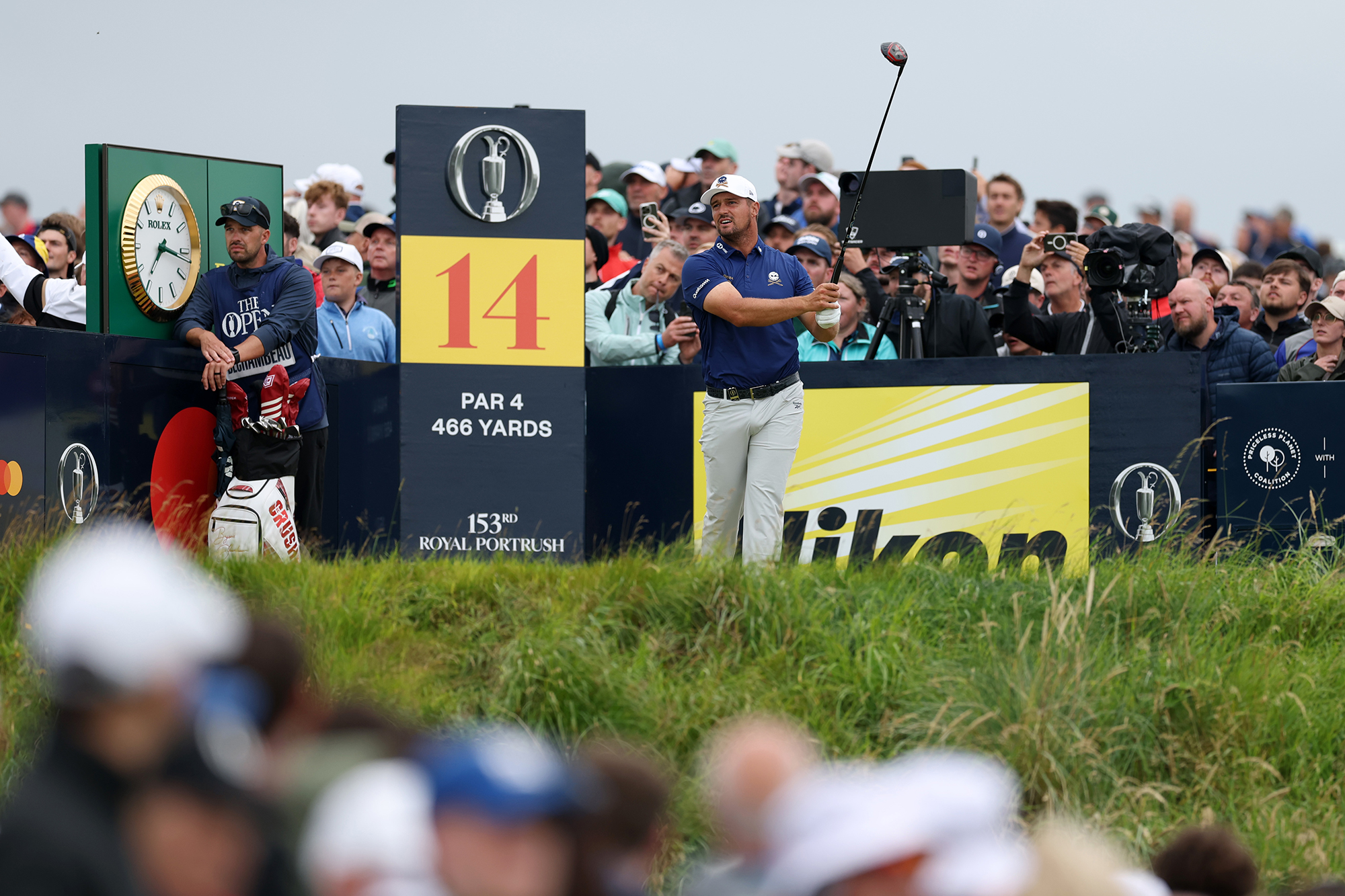 Bryson DeChambeau in the finish position after hitting driver off the tee during round one of the Open Championship at Royal Portrush, watched by a gallery of fans
