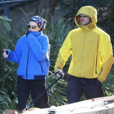 Kendall Jenner and Jacob Elordi walk a dog outside wearing technical jackets in blue and yellow. Kendall wears a bandana on her head and the two shield their eyes with sunglasses.