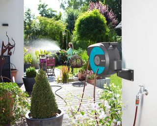 Wall mounted garden hose reel and woman hosing her plants