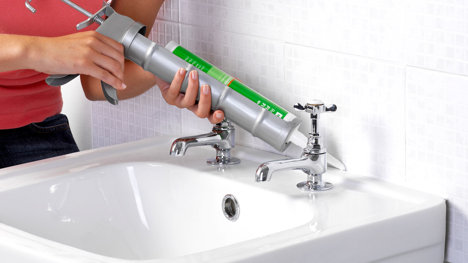 Silver caulk gun applying white bathroom sealant to white bathroom sink