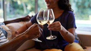Woman drinking glass of wine with friend on sofa