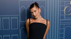 Hailey Bieber in a black dress against a dark blue patterned wall