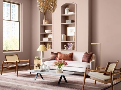 A living room painted pale pink with a cream sofa, rattan chairs, and alcove shelving 