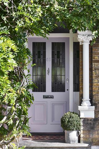 Traditional brick house with pale purple door surrounded by greenery