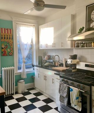 A kitchen with white and blue walls, black and white tiled flooring, white cabinets, an oven, and a kitchen trash can