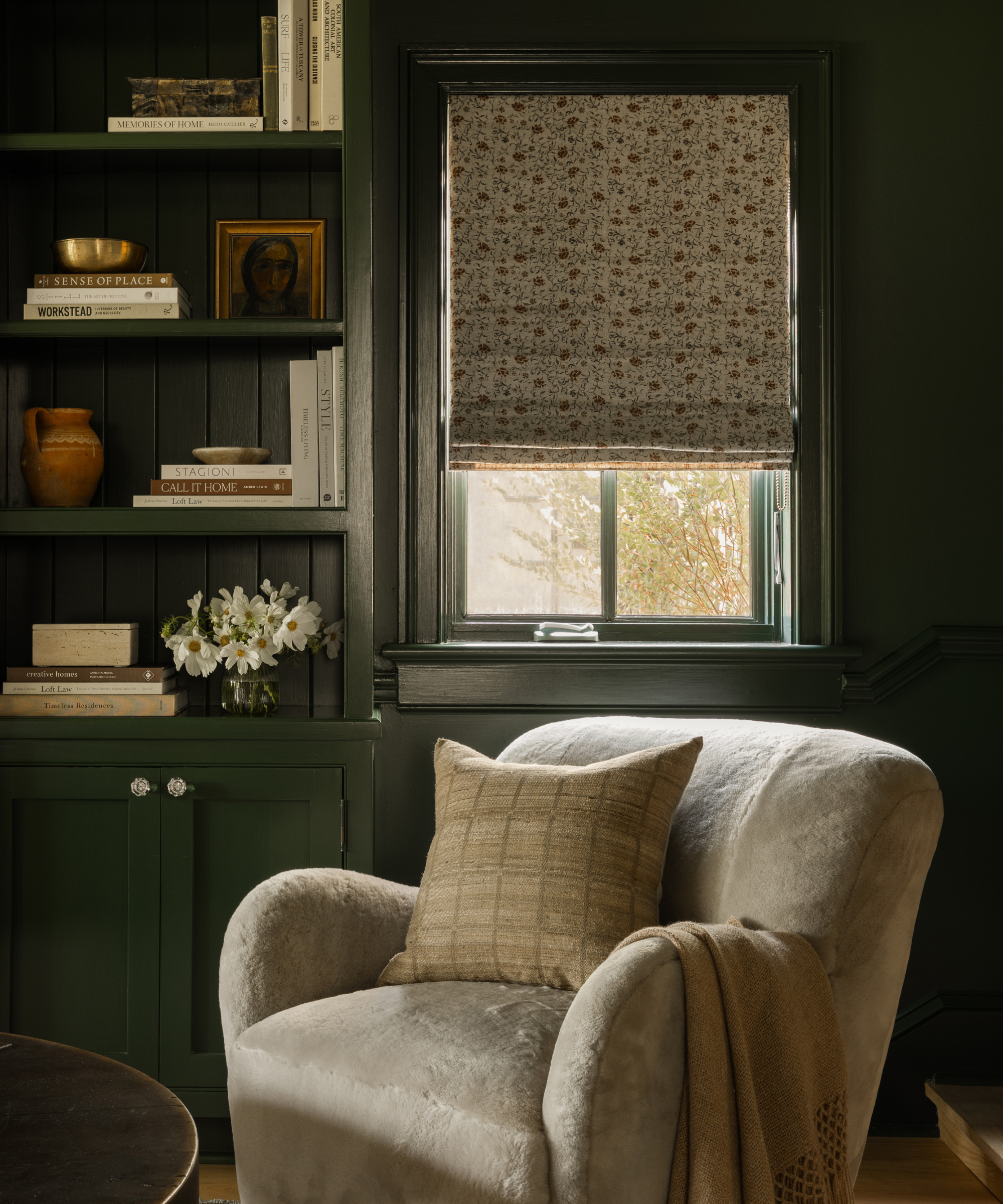 a cozy sitting area with a chair, a wall of shelves and books, and a window with a curtain