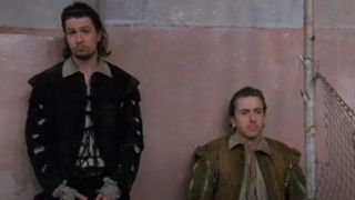 Gary Oldman standing and Tim Roth sitting against a wall in Rosencrantz & Guildenstern Are Dead.