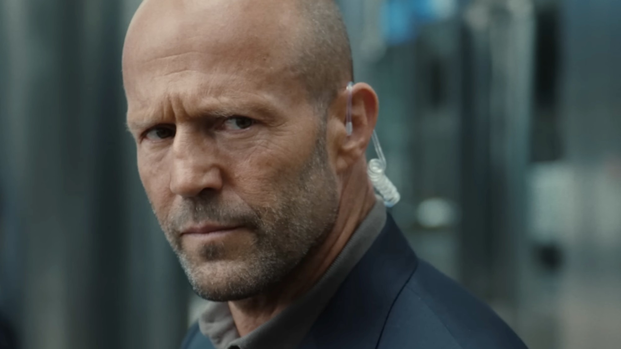 A close up of Jason Statham with an ear piece in.